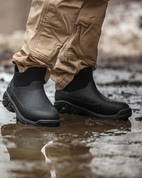 A man wearing a pair of Muck Boots, walking through the mud