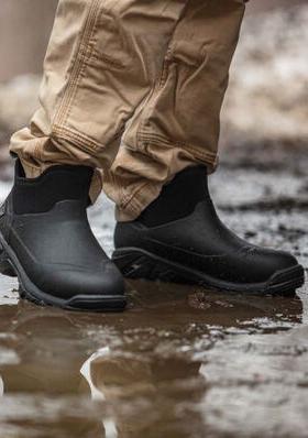 A man wearing a pair of Muck Boots, walking through the mud
