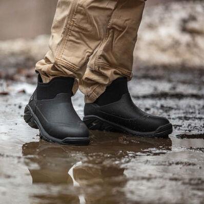 A man wearing a pair of Muck Boots, walking through the mud