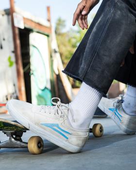 A man skateboarding wearing a cream pair of Lakai shoes with a baby blue logo