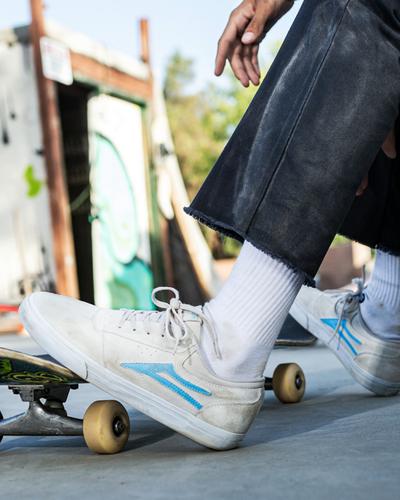 A man skateboarding wearing a cream pair of Lakai shoes with a baby blue logo