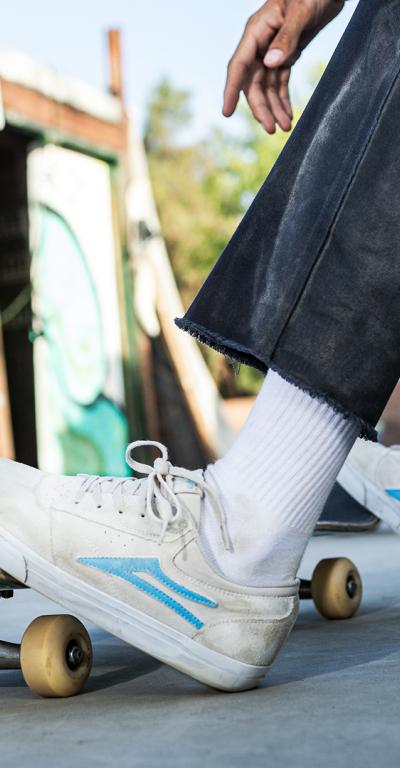 A man skateboarding wearing a cream pair of Lakai shoes with a baby blue logo