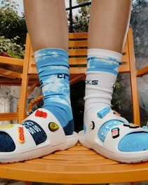 A person wearing white Crocs with little designs on top of them