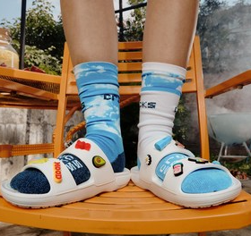 A person wearing white Crocs with little designs on top of them