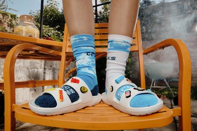 A person wearing white Crocs with little designs on top of them