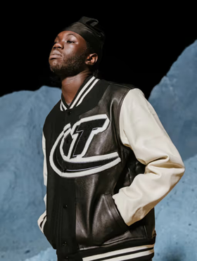 A man wearing a coaches varsity jacket by Trapstar