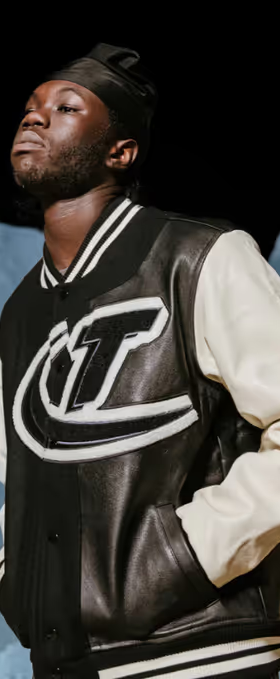 A man wearing a coaches varsity jacket by Trapstar