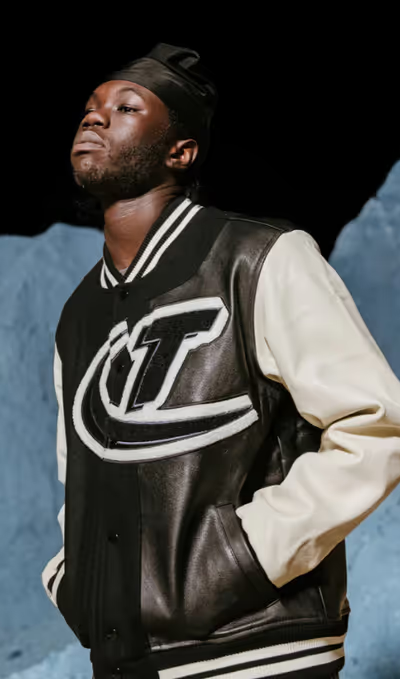 A man wearing a coaches varsity jacket by Trapstar