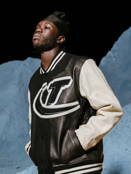 A man wearing a coaches varsity jacket by Trapstar
