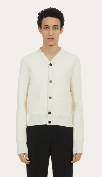 A man wearing a white Ferragamo cardigan and black pants