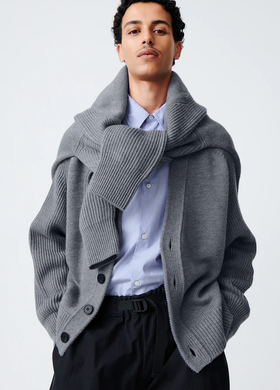 A man wearing a Studio Nicholson grey cardigan with a sweater wrapped around his neck