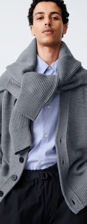 A man wearing a Studio Nicholson grey cardigan with a sweater wrapped around his neck