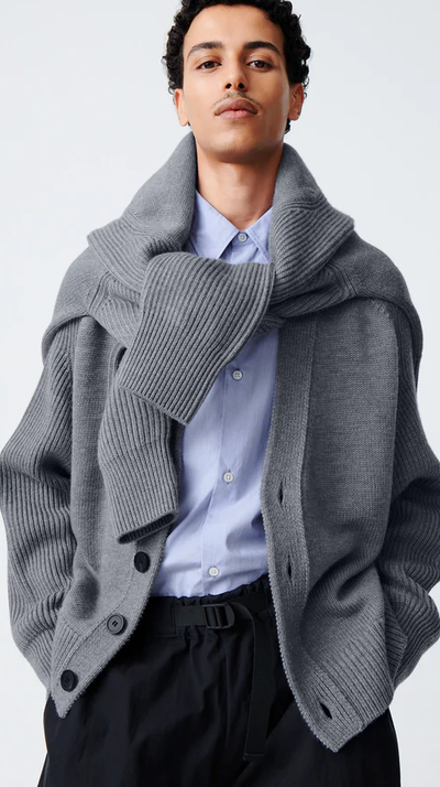A man wearing a Studio Nicholson grey cardigan with a sweater wrapped around his neck
