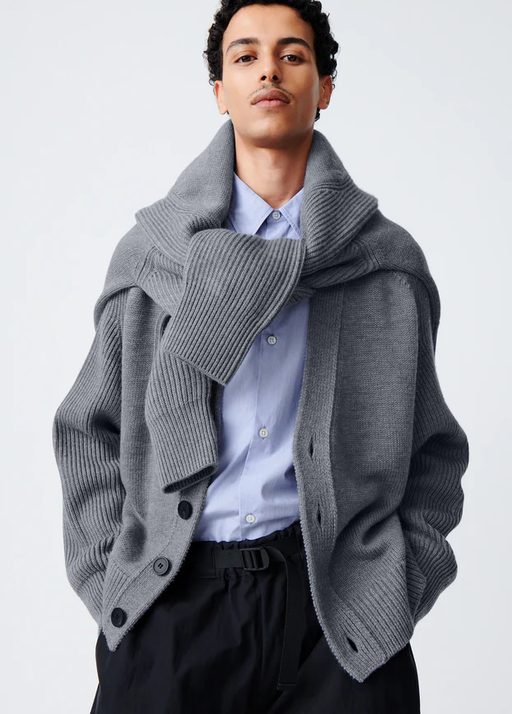 A man wearing a Studio Nicholson grey cardigan with a sweater wrapped around his neck