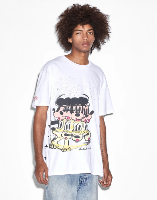 A man wearing a Ksubi graphic t-shirt in white with blue jeans