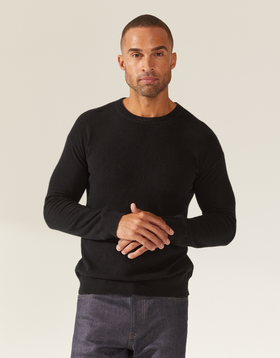 A man wearing a tight-fitting black Italic sweater and grey jeans