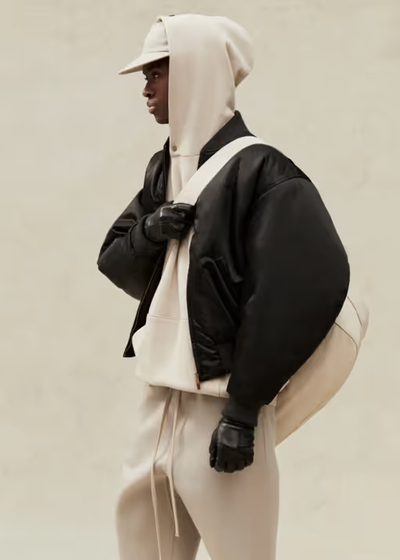 A man wearing a cream Fear of God Essentials hoodie, jacket and matching sweatpants