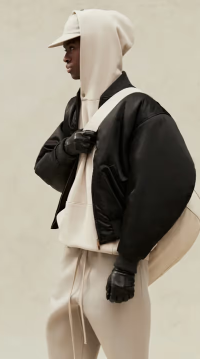 A man wearing a cream Fear of God Essentials hoodie, jacket and matching sweatpants