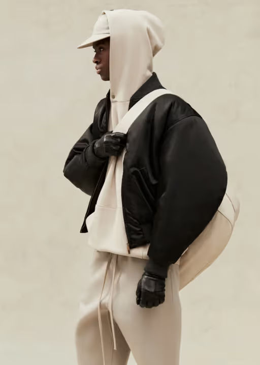 A man wearing a cream Fear of God Essentials hoodie, jacket and matching sweatpants