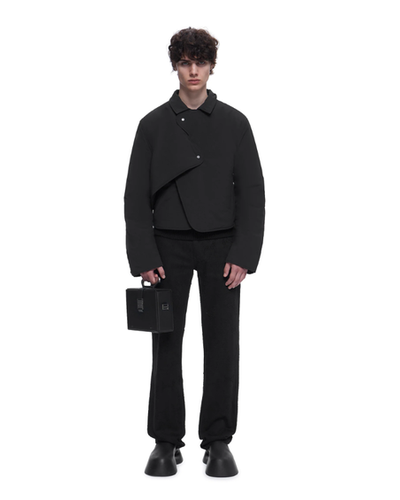 A man wearing a HELIOT EMIL outfit in all black with a black purse