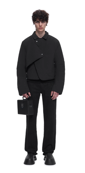 A man wearing a HELIOT EMIL outfit in all black with a black purse