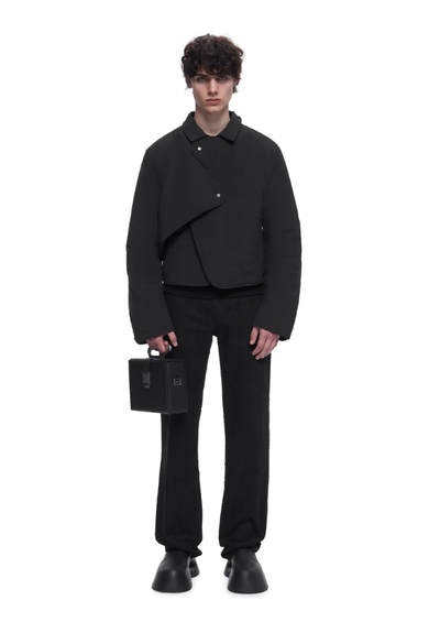 A man wearing a HELIOT EMIL outfit in all black with a black purse