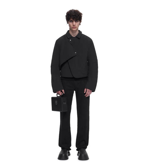 A man wearing a HELIOT EMIL outfit in all black with a black purse