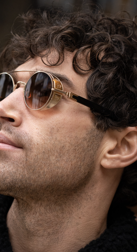 A man wearing a pair of Matsuda gold-rimmed circular sunglasses