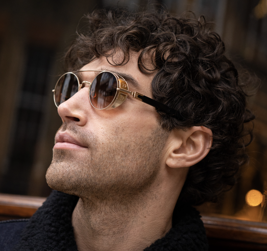 A man wearing a pair of Matsuda gold-rimmed circular sunglasses