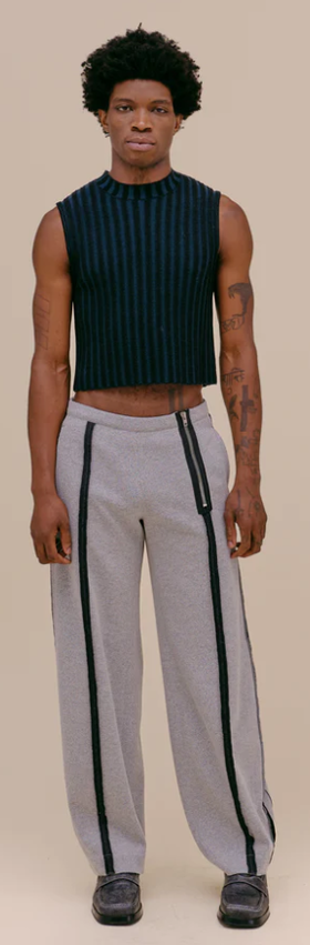 A man wearing a tight fitting Eckhaus Latta shirt with oversize grey pants