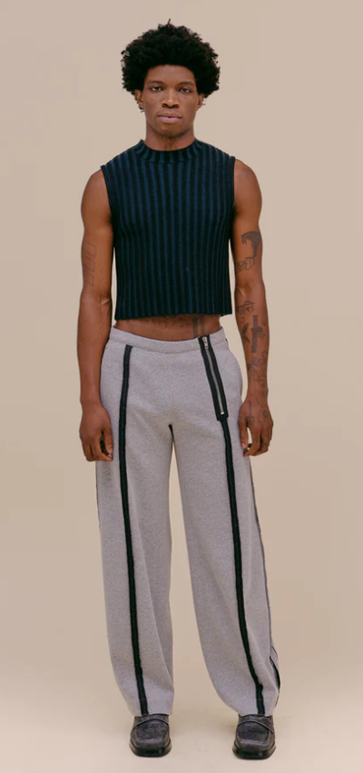 A man wearing a tight fitting Eckhaus Latta shirt with oversize grey pants
