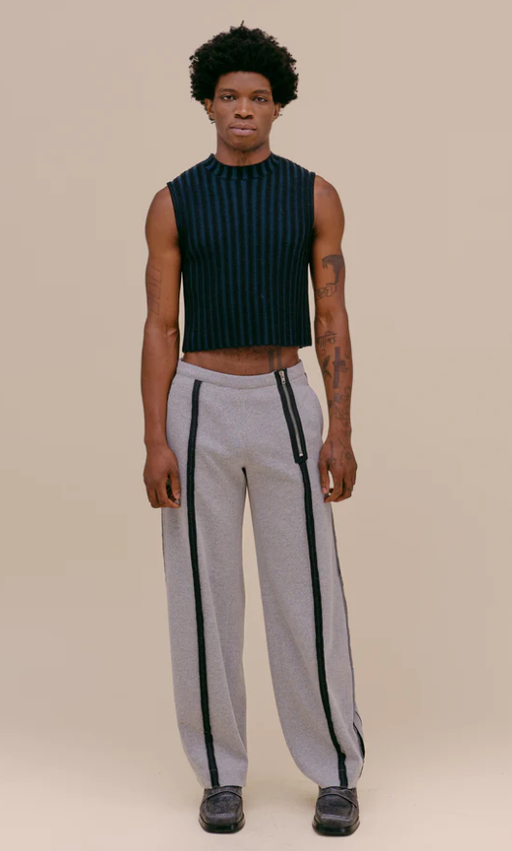 A man wearing a tight fitting Eckhaus Latta shirt with oversize grey pants
