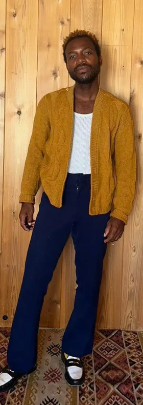 A man wearing a Depop orange sweater and black pants