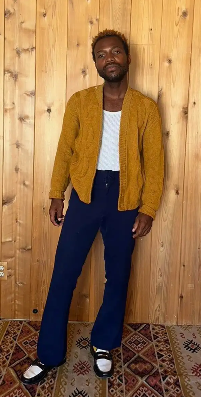 A man wearing a Depop orange sweater and black pants