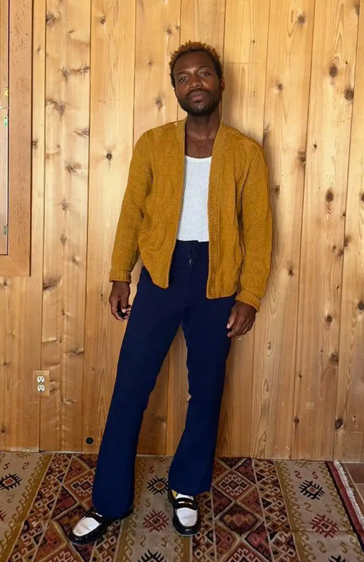 A man wearing a Depop orange sweater and black pants