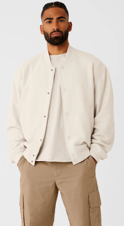 A man wearing a cream Alo bomber jacket and brown pants