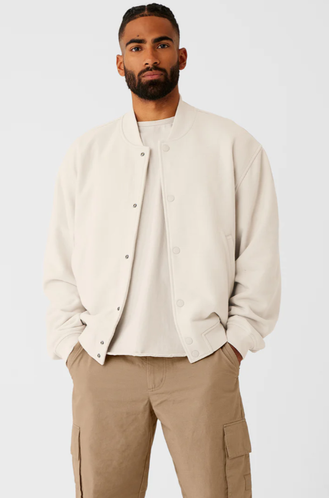 A man wearing a cream Alo bomber jacket and brown pants