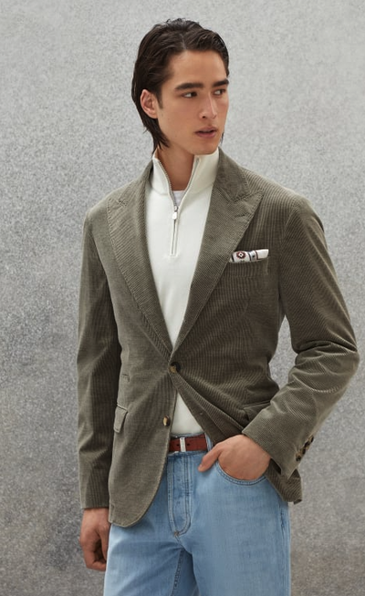 A man wearing a slick, tight-fitting Brunello Cucinelli olive suit jacket with white zip sweater beneath it