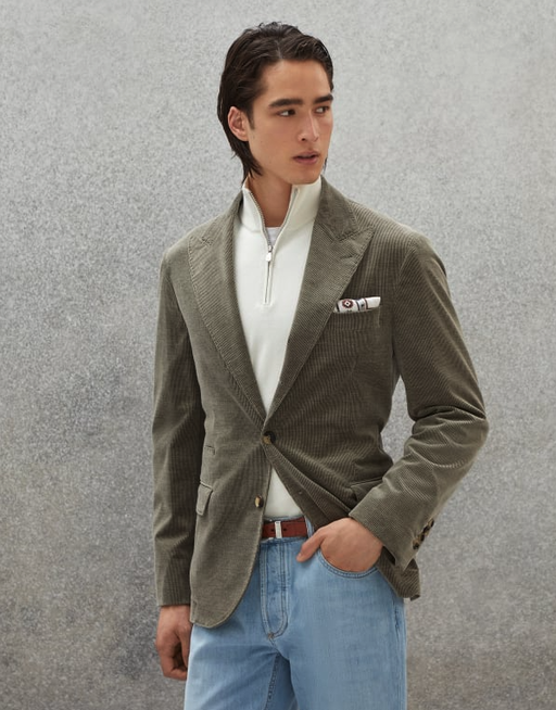 A man wearing a slick, tight-fitting Brunello Cucinelli olive suit jacket with white zip sweater beneath it