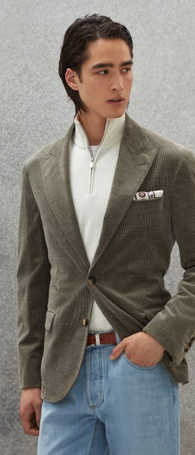 A man wearing a slick, tight-fitting Brunello Cucinelli olive suit jacket with white zip sweater beneath it