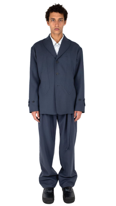 A man wearing a dark navy Kiko Kostadinov suit