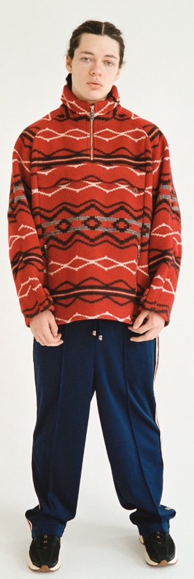 A man wearing a red TTTMSW sweater and black pants