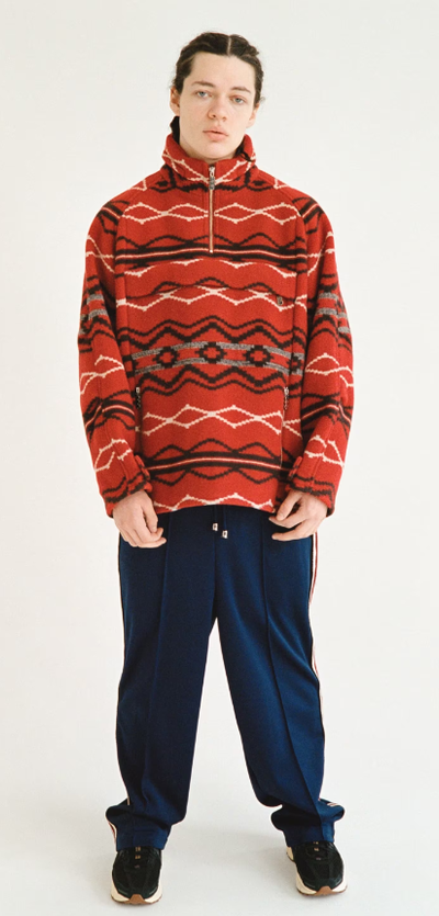 A man wearing a red TTTMSW sweater and black pants