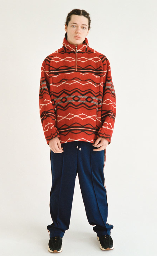 A man wearing a red TTTMSW sweater and black pants