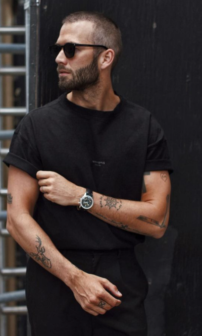 A man wearing a Breitling watch with a black t-shirt and sunglasses