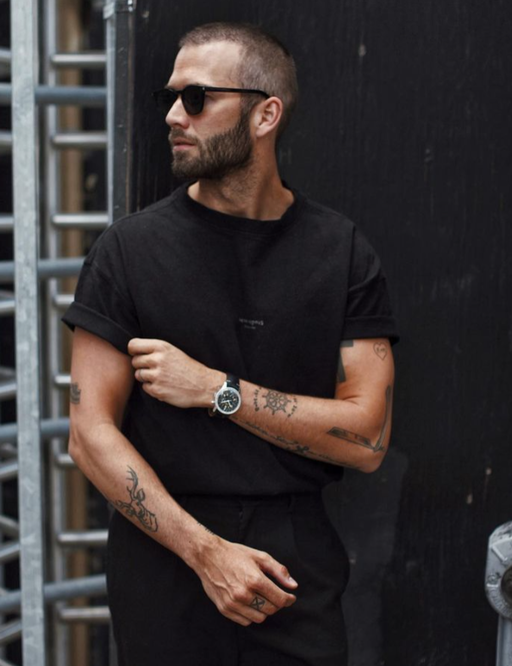 A man wearing a Breitling watch with a black t-shirt and sunglasses