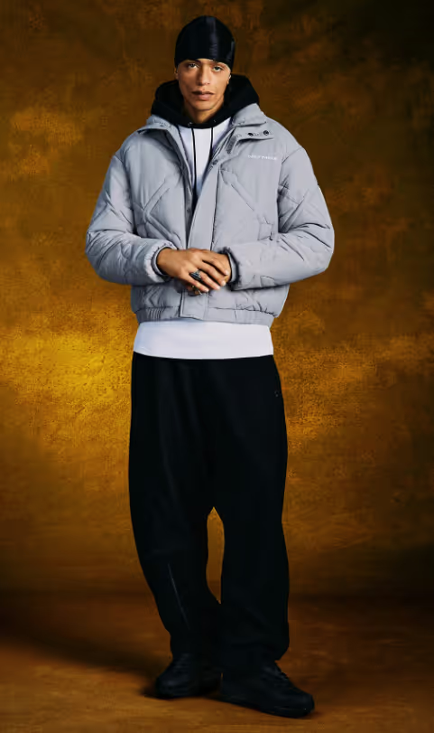 A man wearing a Daily Paper outfit with a grey jacket and white shirt