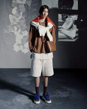 A man wearing a Denim Tears outfit with a brown jacket and white shorts