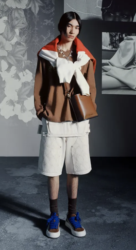 A man wearing a Denim Tears outfit with a brown jacket and white shorts