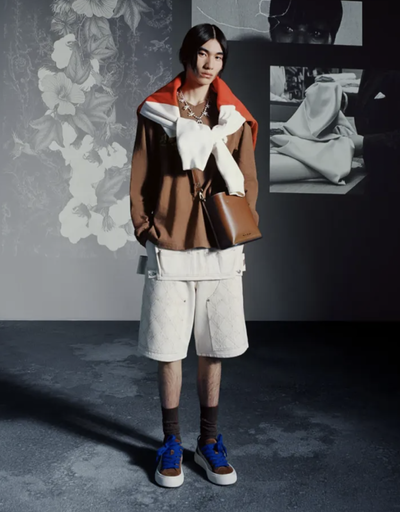 A man wearing a Denim Tears outfit with a brown jacket and white shorts